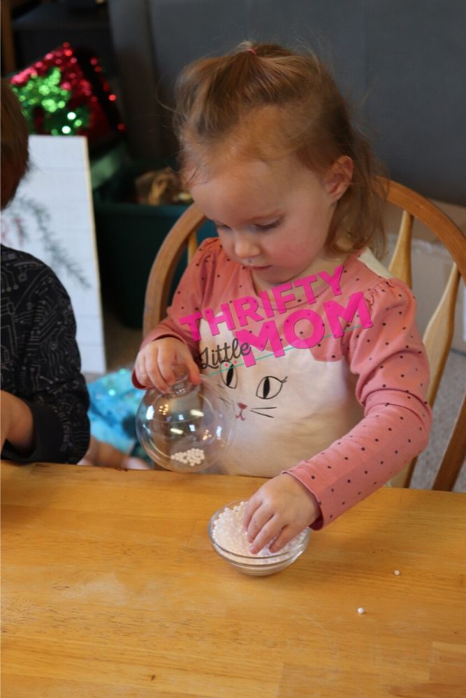 toddler putting snowballs in cricut ornament