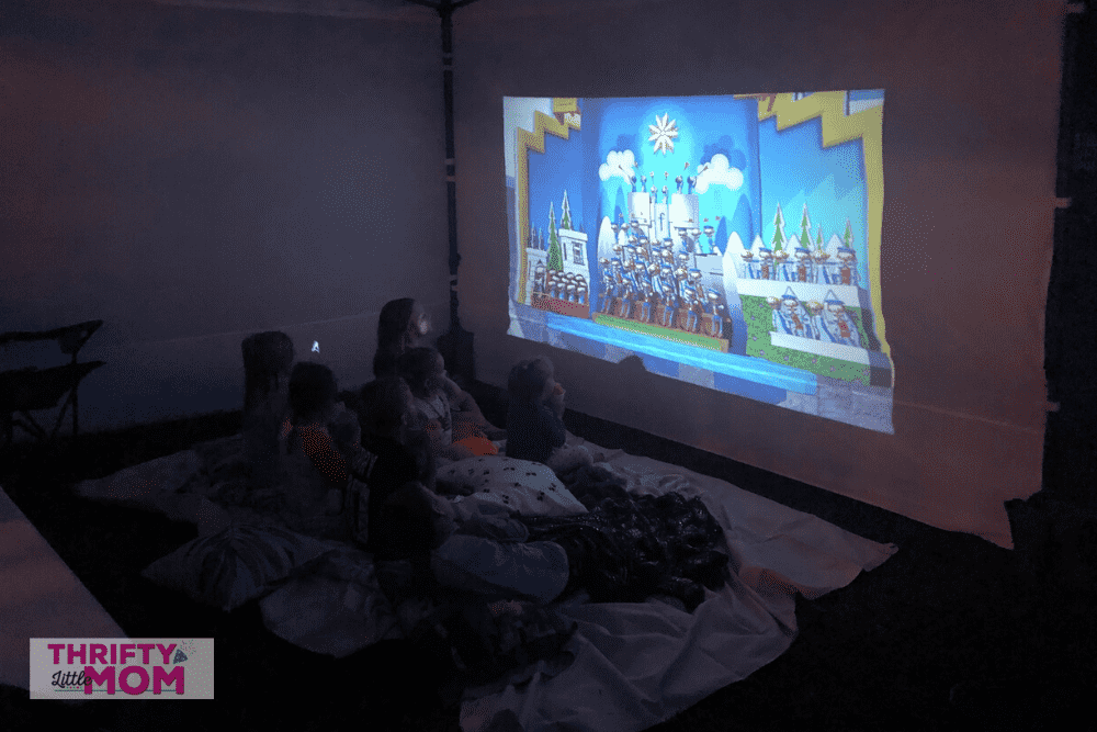 Thrifty little Moms Halloween backyard movie party. Kids on a blanket watching a movie on a big screen projector.